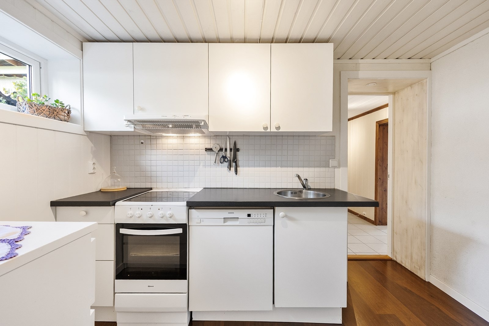 Kjøkkenet i underetasjen er fra 2011, har MDF-plater på veggene, parkett på gulv og innredning med hvite, glatte fronter og nedfelt oppvaskkum i laminatbenkeplate. Galleribilde