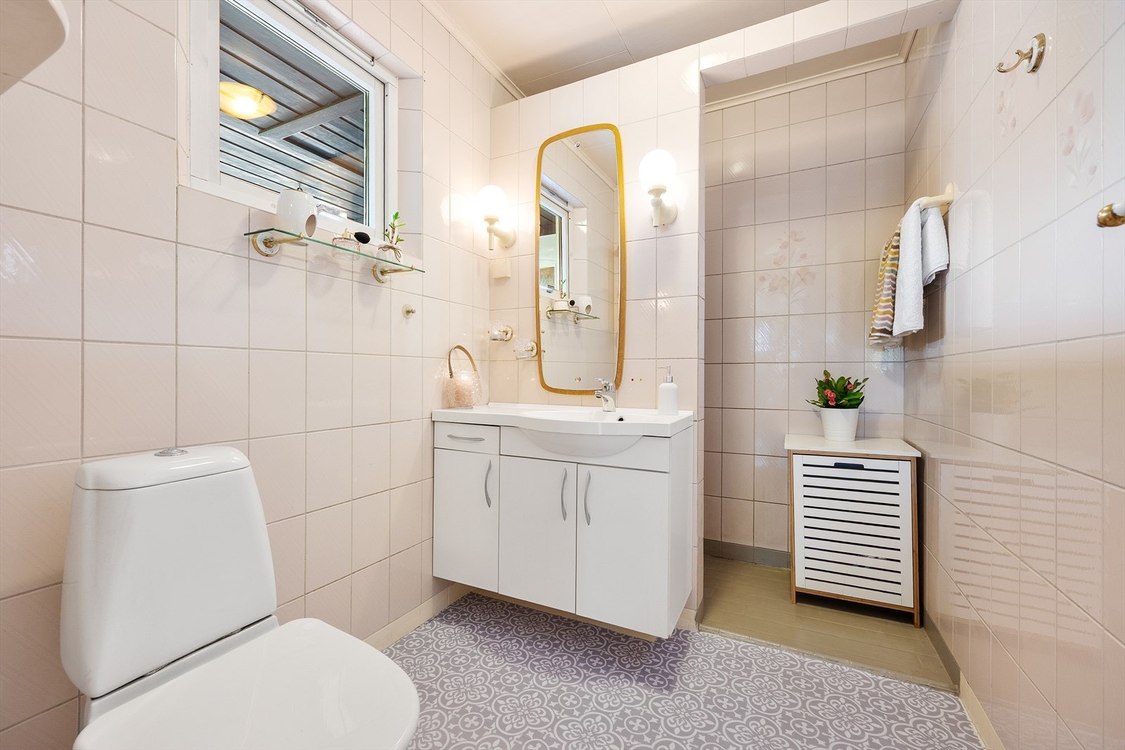 Det helflisede badet er i lyse fargetoner og har lun gulvvarme. Innredningen har heldekkende servant over skapseksjon med speil i overkant. Flisene i dujsnisjen er malt over med Epoxy maling, og de øvrige flisene er belagt med enkle vinylfliser. Galleribilde