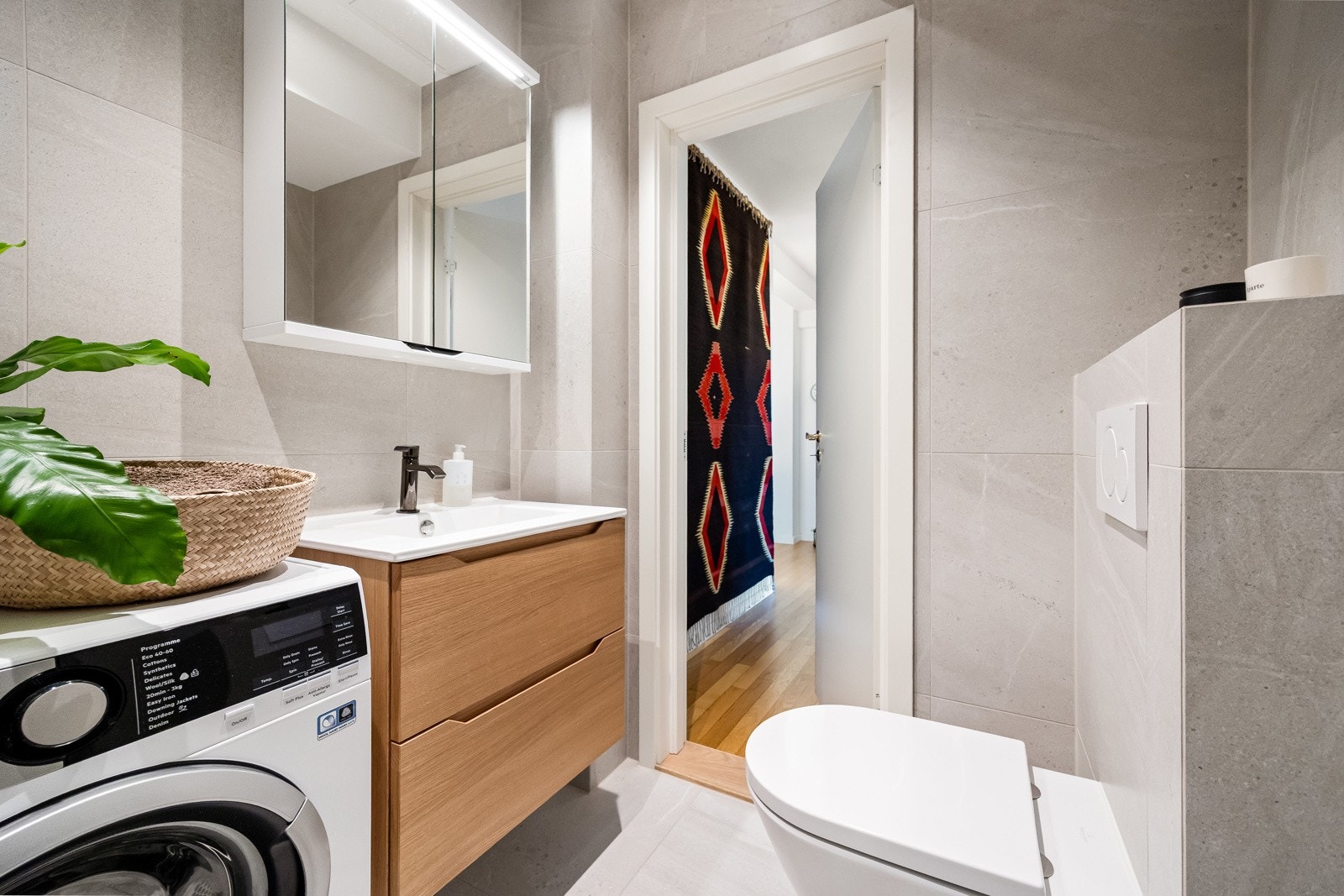 Badet er velutnyttet og inneholder servantinnredning med speilskap, dusjnisje, vegghengt toalett og opplegg for vaskemaskin Galleribilde