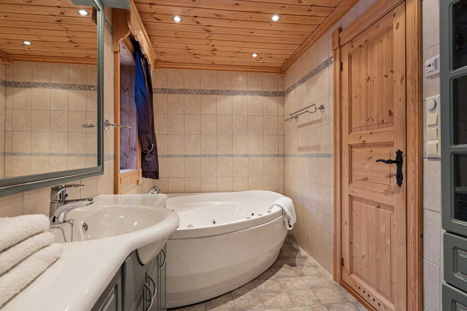 Badet er innredet med toalett, dusjsnisje med glassvegger, boblekar med dysefunksjon, baderomsinnredning med heldekkende servant, tilhørende høyskap og speil med belysning. Galleribilde