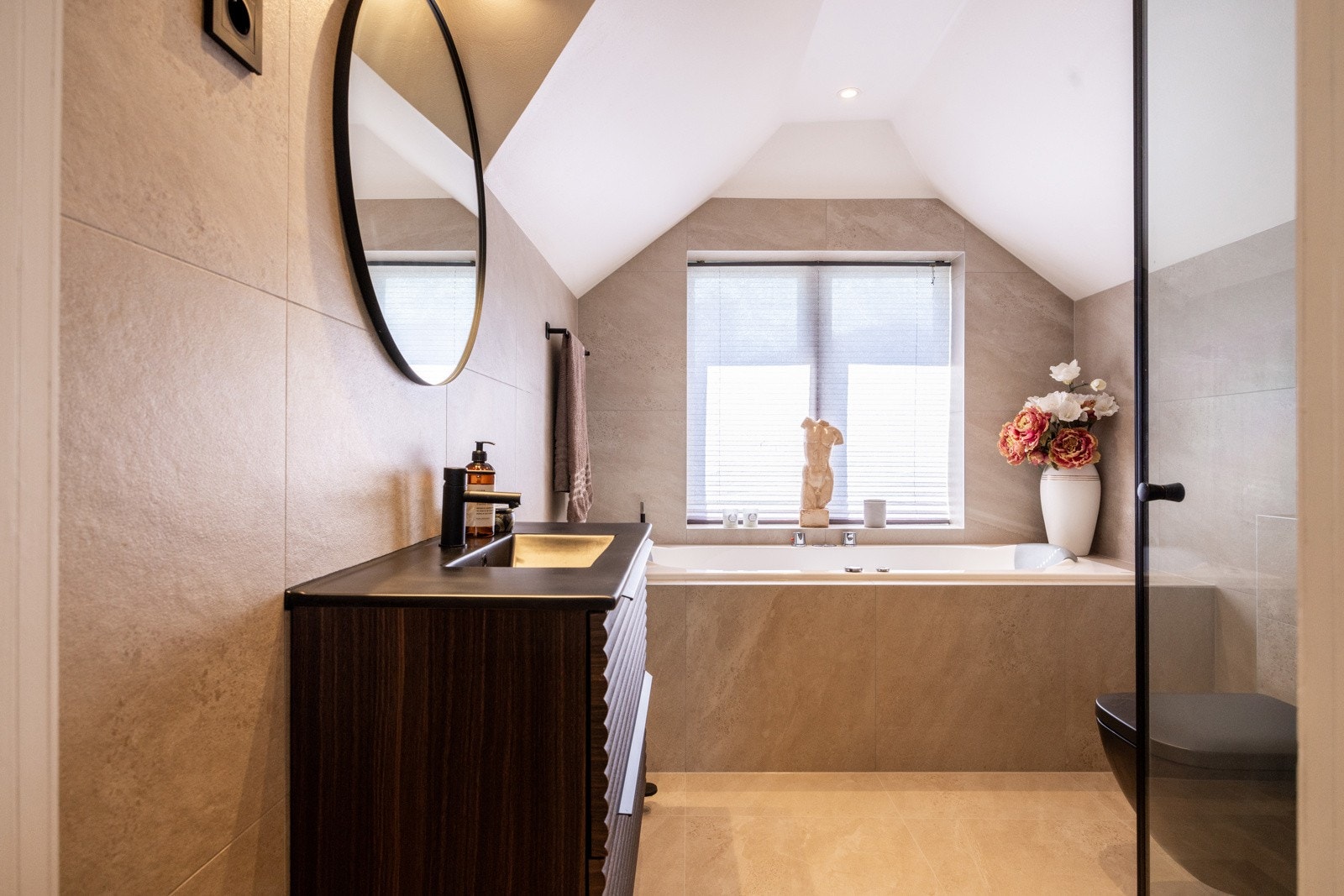 Pent flislagt bad. Baderomsinnredningen består av servantskap med skuffer samt nedfelt servant, i tillegg til et vegghengt speil plassert over servanten. Videre er det dusjhørne, badekar og vegghengt toalett med innebygd sisterne. Galleribilde