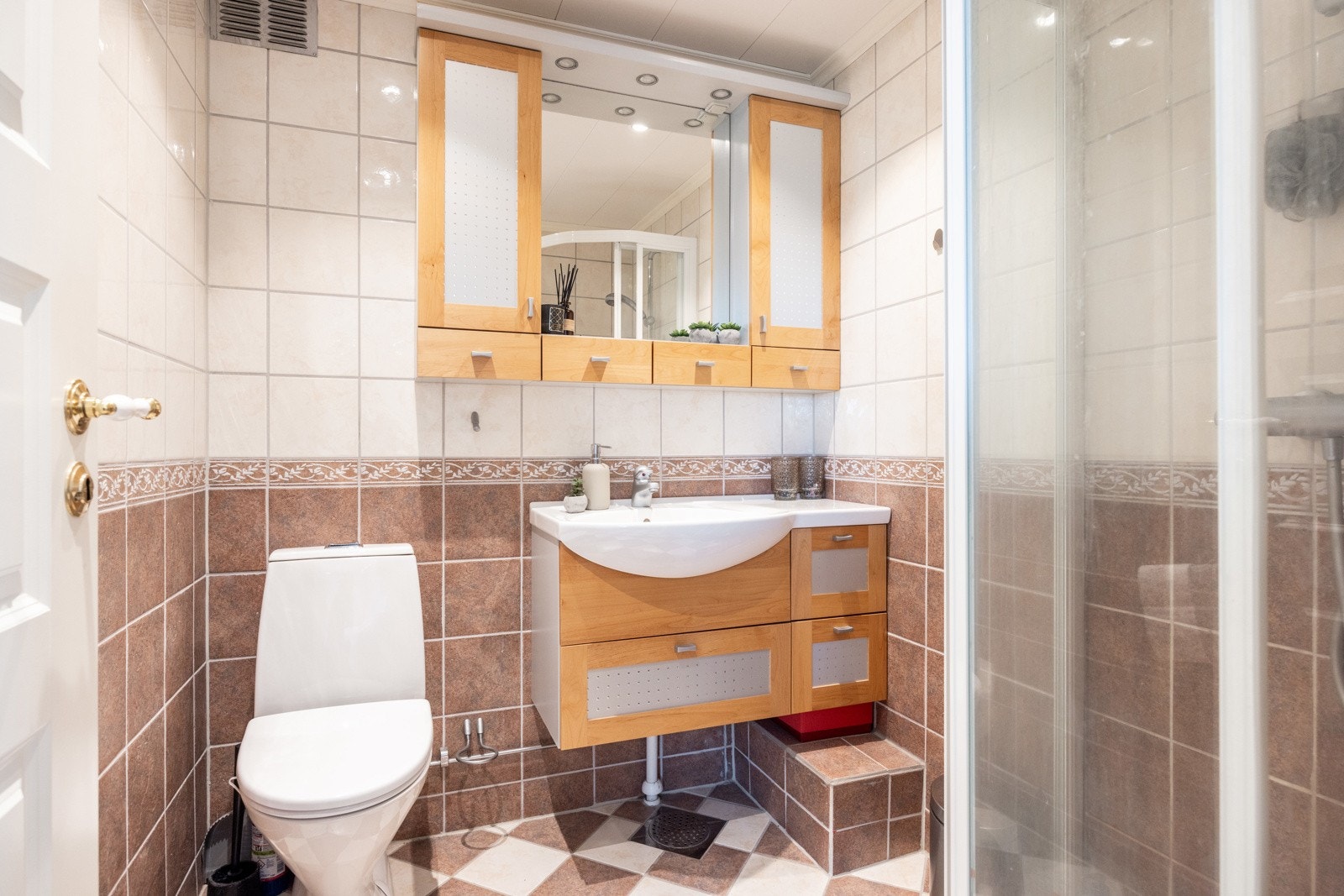 Bad med flis på vegg og gulv, malte plater i taket. Rommet er innredet med dusjhjørne, servant i innredning og toalett. Galleribilde