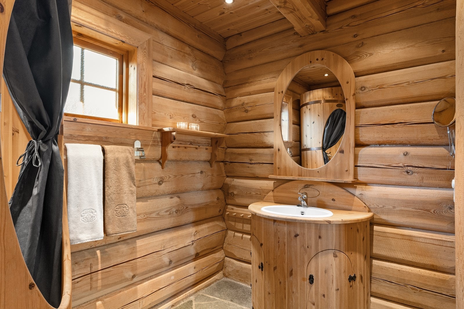 Badet har solide laftevegger, og skifer på gulvet med elektrisk gulvvarme. Det er servant med spesialbygd innredning med skap og speil over. Det er downlights i himlingen. Galleribilde