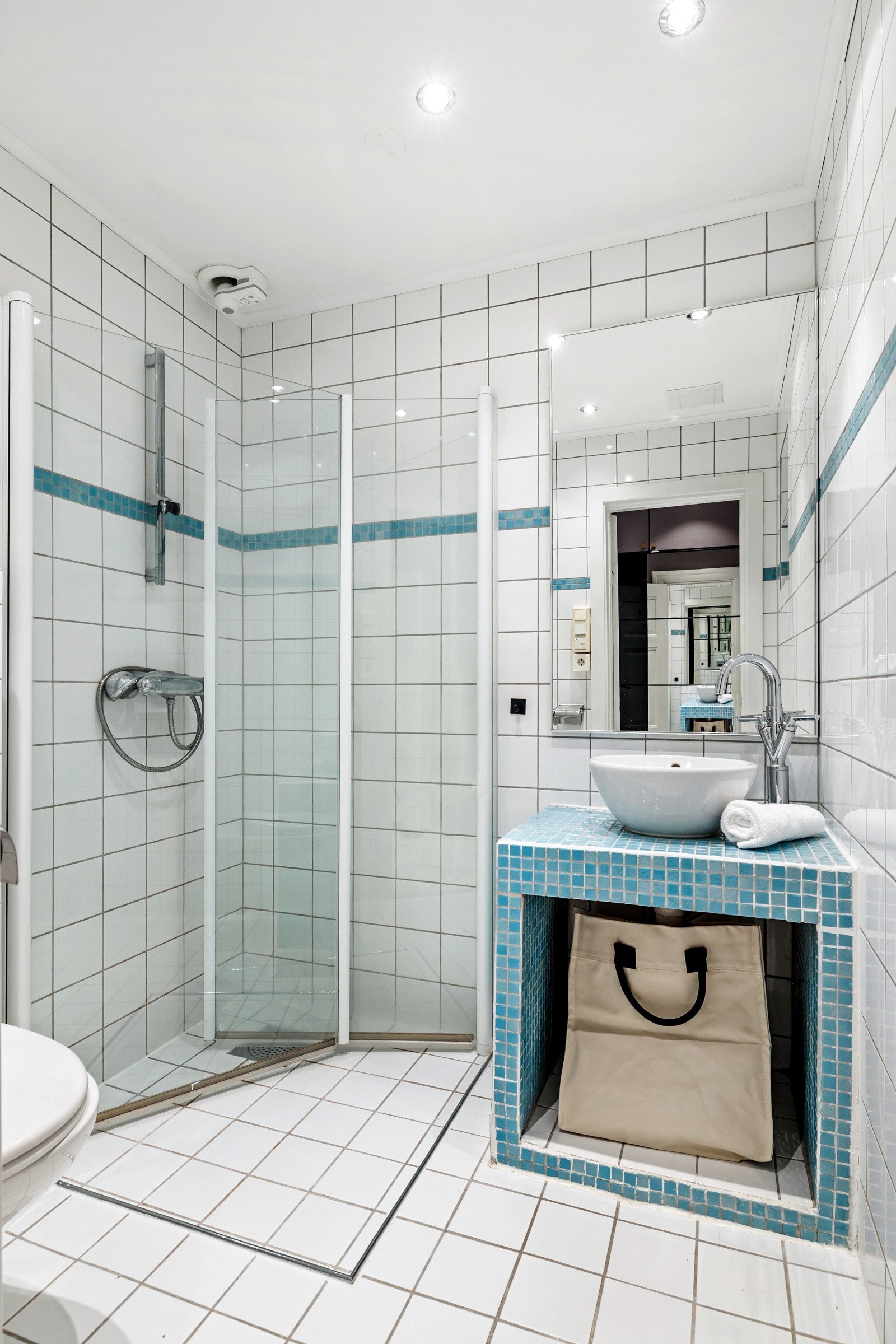 Badet er innredet med oppmurt benk, hvit servant, speil, dusjhjørne og toalett. Galleribilde