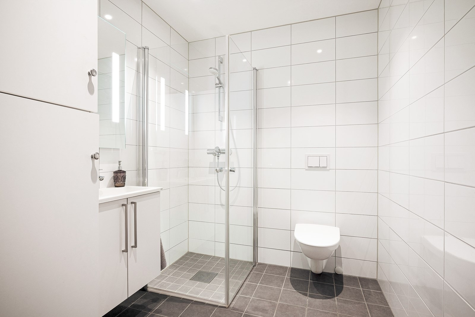 Moderne og stilrent bad i 1. etasje med flislagte vegger og gulv. Praktisk dusjløsning og vegghengt toalett for enkel rengjøring. Galleribilde