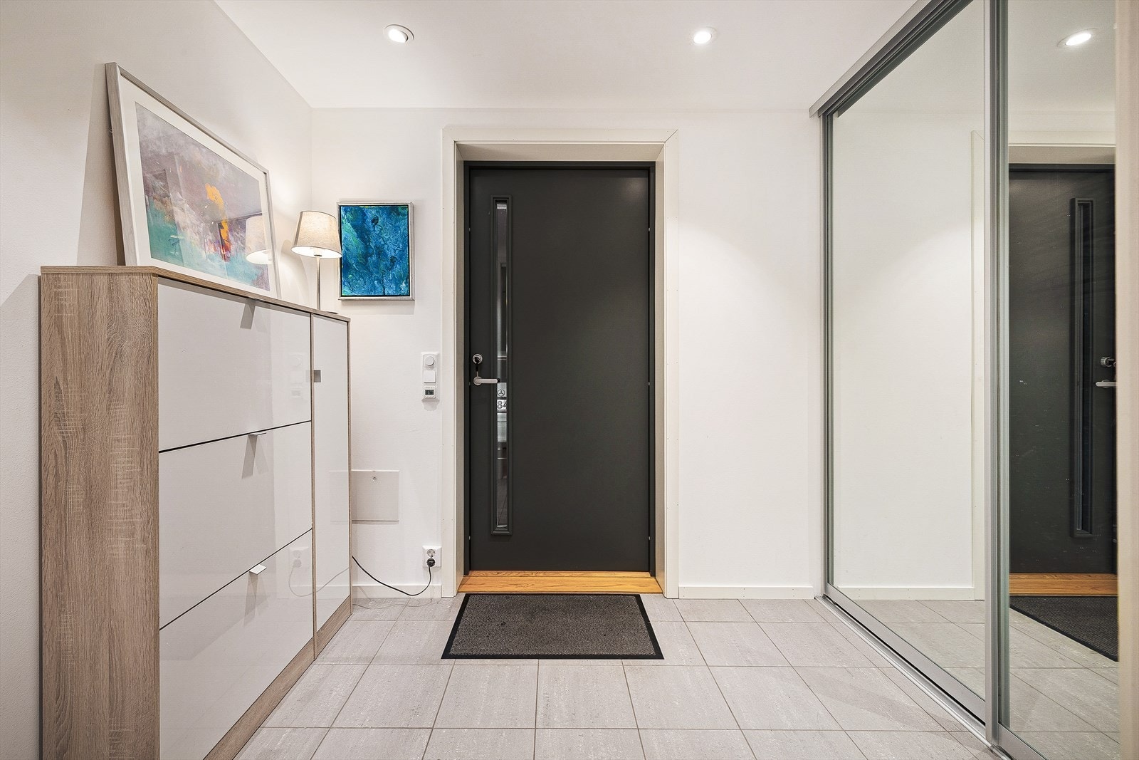 Velkommen til en moderne og innbydende entré med stilren design og praktiske løsninger. Plass til å henge fra seg yttertøy og sko i skyvedørsgarderobe med speilfronter. Galleribilde
