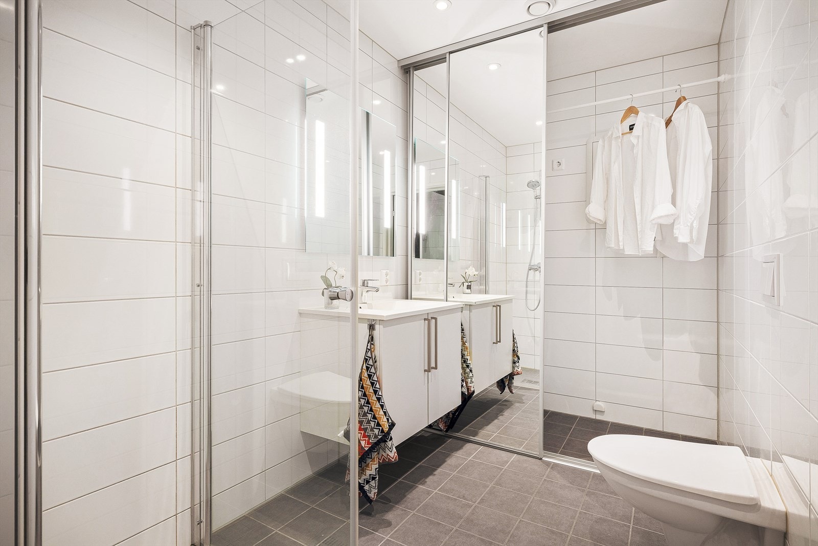 Lyst og moderne bad med romslig dusjløsning. Vaskemaskin og tørketrommel kan skjules bak skyvedørsfronter med speilfront. Galleribilde