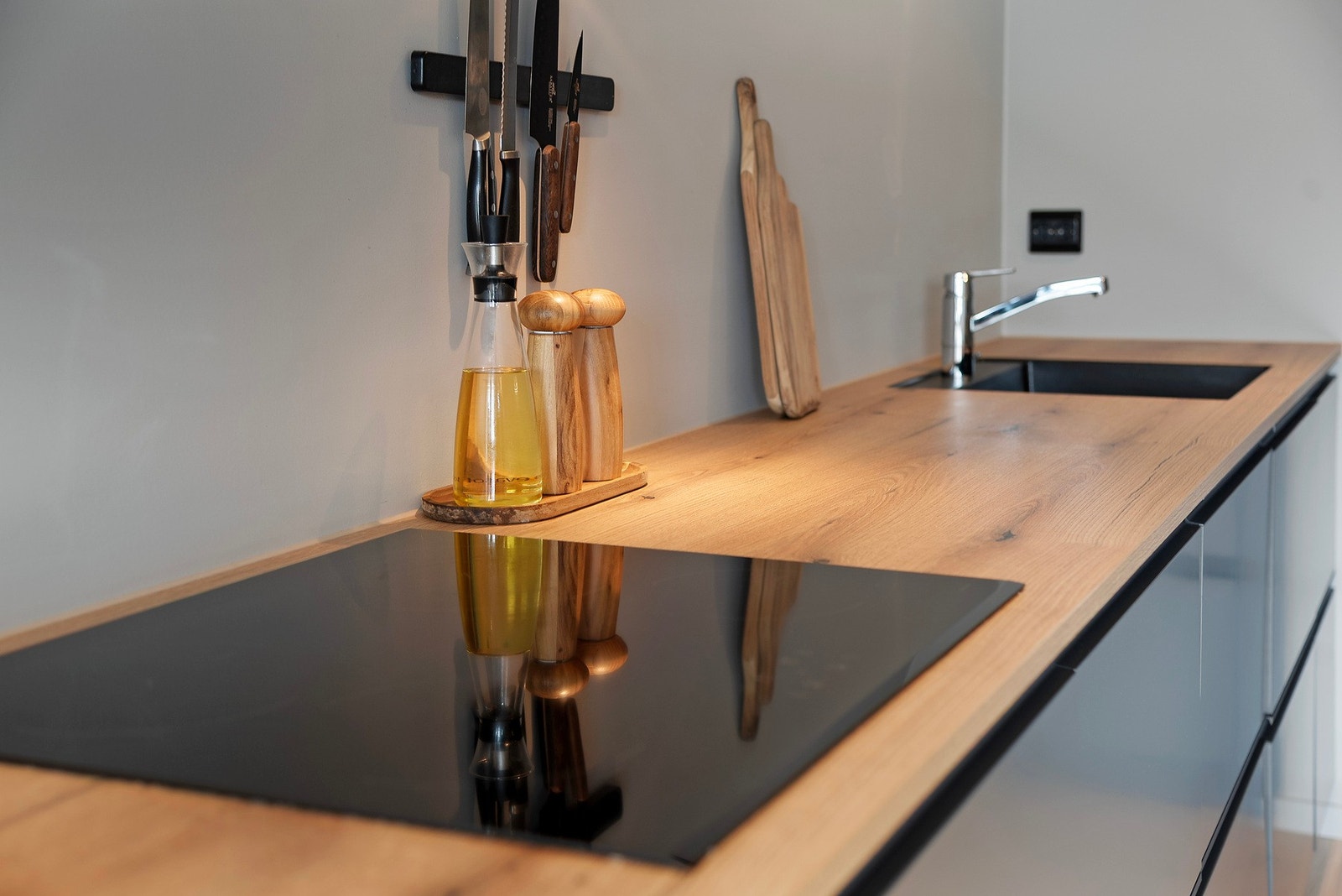 Benkeplaten harmonerer med gulvet og skaper en helhetlig stil på kjøkkenet, mens den svarte nedfelte servanten og integrerte platetoppen forsterker det moderne og rene uttrykket Galleribilde