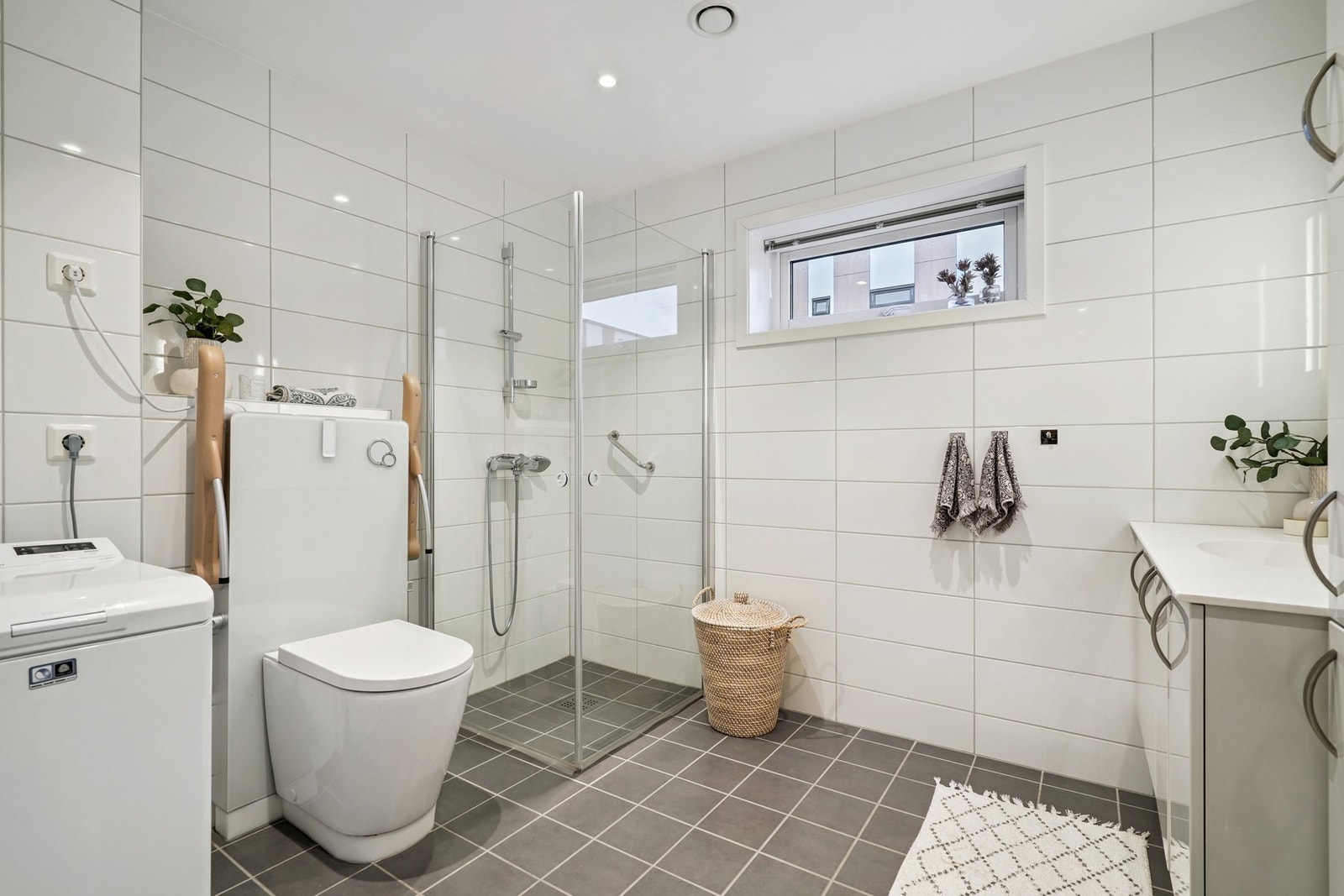 Lyst helfliset bad/vaskerom med vannbåren gulvvarme. I hvit himling er det downlights med dimming. Galleribilde