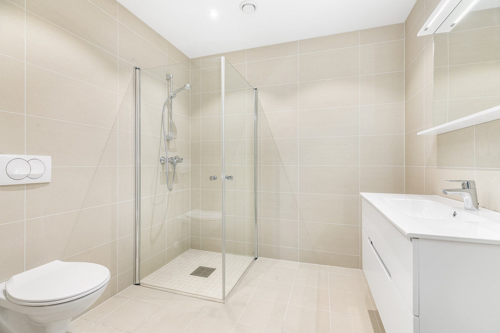 Fliser i lik fargenyanse på gulv og vegger fremmer helhet på badet. LED-spotter innfelt i himlingen kan dimmes. Galleribilde