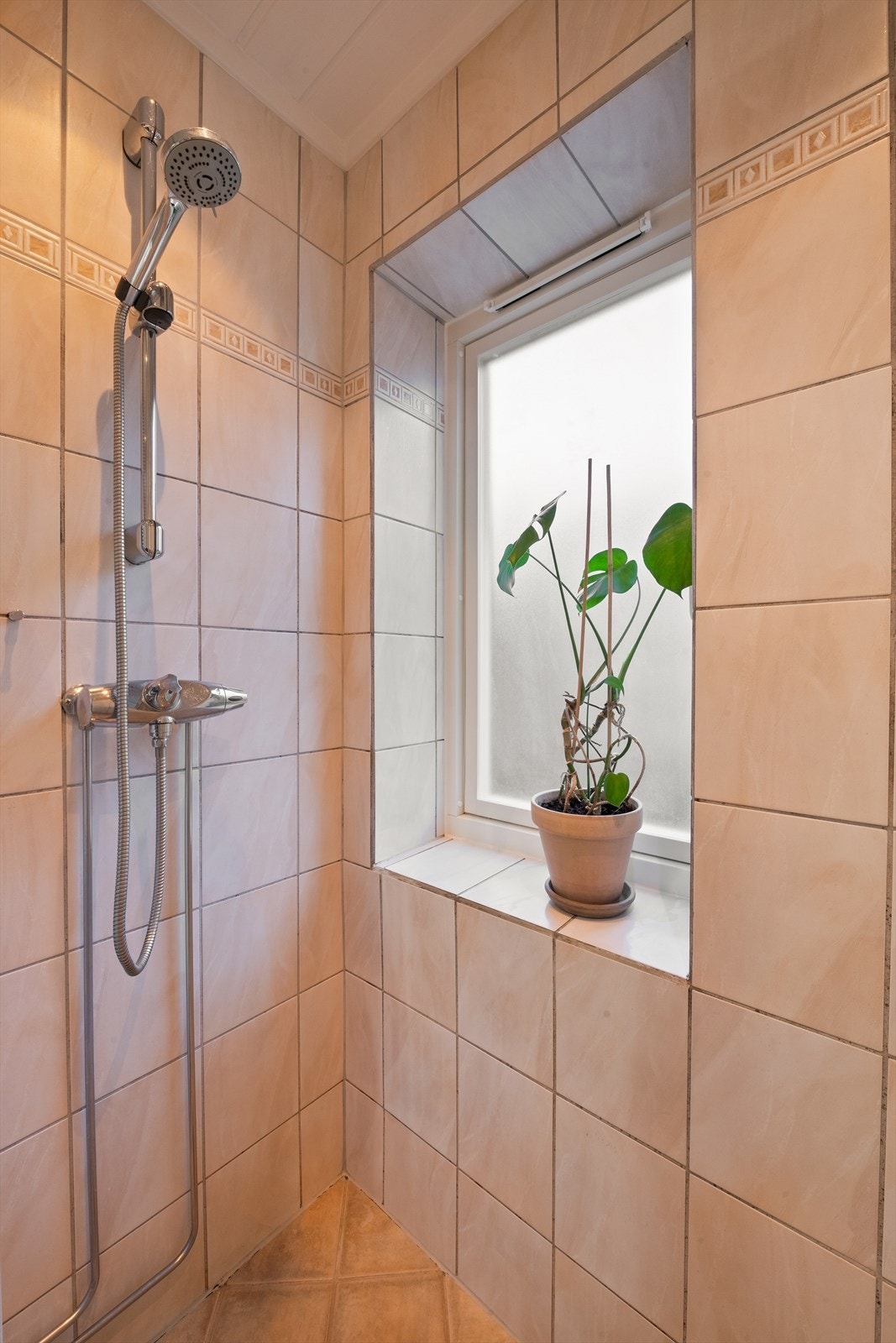 Rommet er innredet med gulvstående toalett, vegghengt servant i praktisk servantskap og dusjvegger i glass som gir en moderne og åpen følelse. Galleribilde