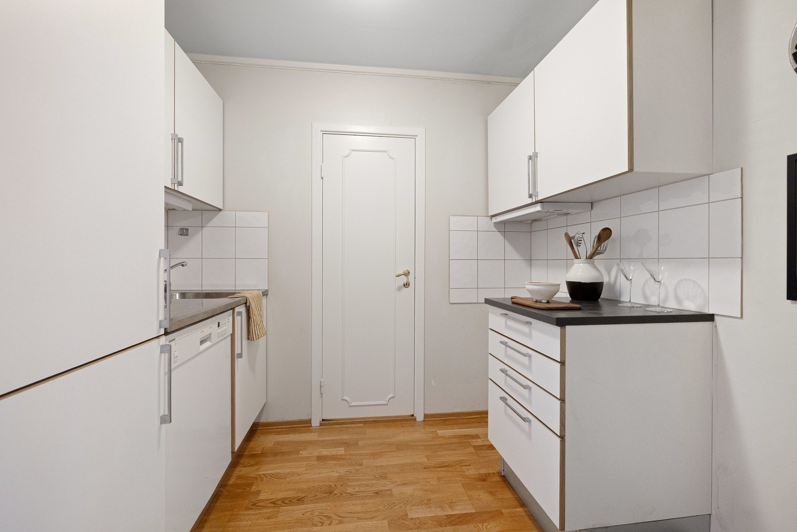 Tvis-kjøkkeninnredning fra 2016 med glatte hvite fronter, mørk laminatbenkeplate og platebeslått. Galleribilde