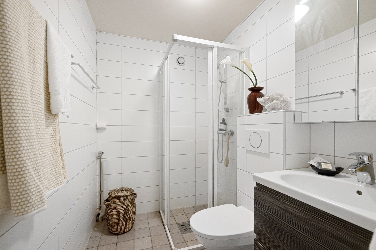 Badet er utstyr med mekanisk avtrekk, opplegg for vaskemaskin, veggmontert toalett og dusjhjørne med gulvskinne, glass-skyvedører og ettgreps dusjbatteri fra Grohe. Galleribilde