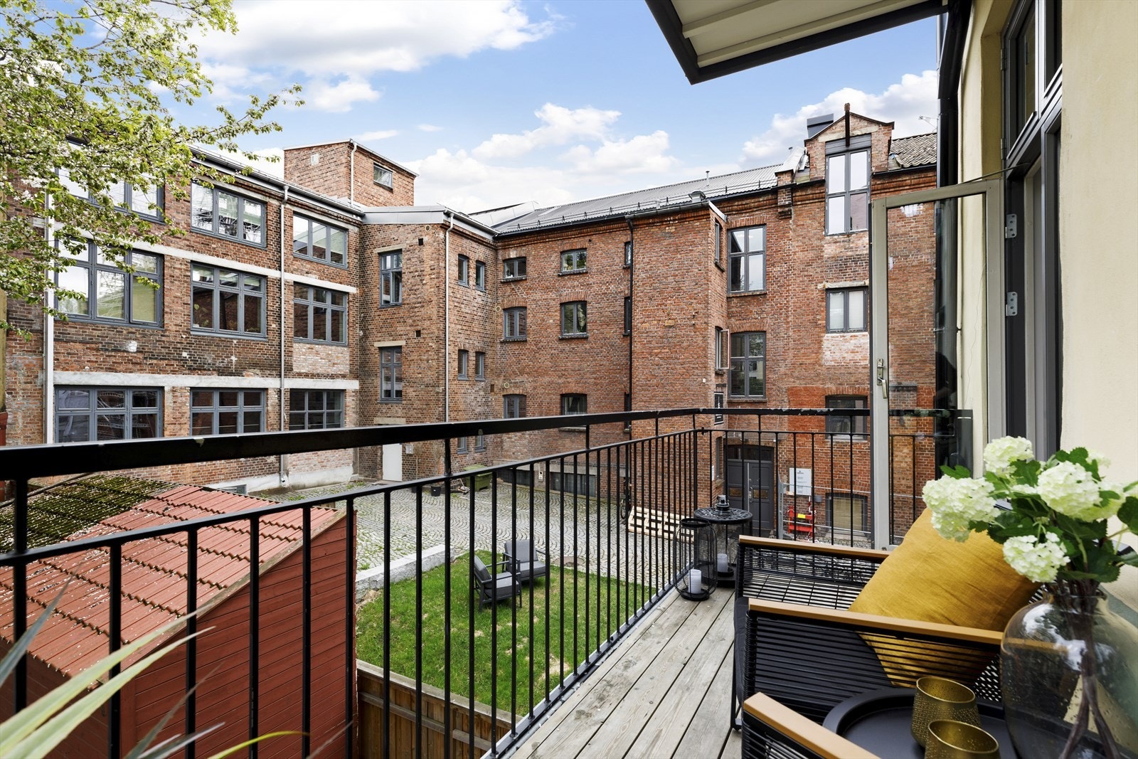 Balkongen gir utsikt mot et koselig gårdsrom med plen og sitteplasser. Galleribilde