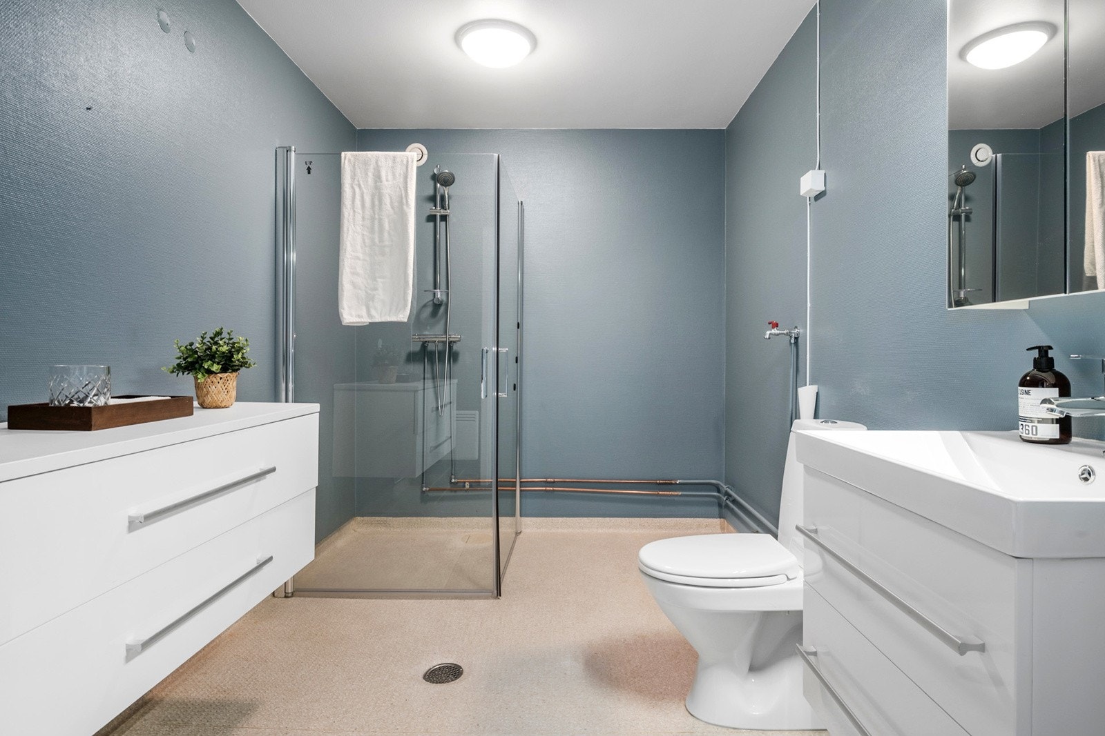 Badet er stort og praktisk og har servant med skuffeseksjon og speil med overlys. Videre har man en tilhørende skuffeseksjon på motsatt side av servanten. Dusjhjørne med svingbare dusjdører Galleribilde