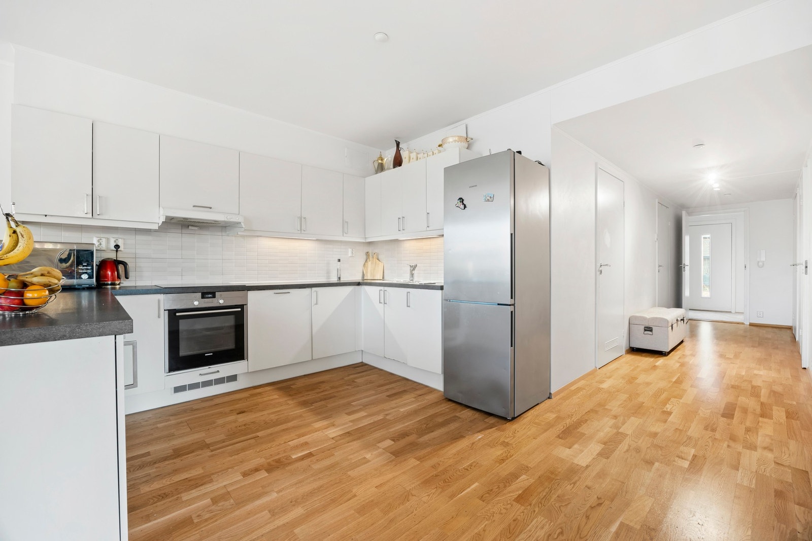 Kjøkkeninnredningen har godt med skap- og benkeplass. Innredningen har slette lakkerte fronter, laminat benk, nedfelt kum, ventilator og fliser på veggen over kjøkkenbenken Galleribilde