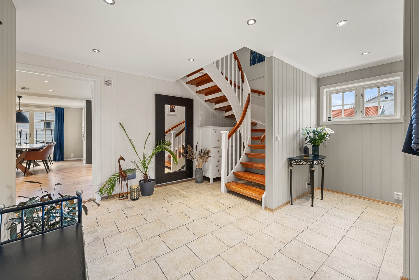 Lys og innbydende hall med fliser på gulv og behagelig gulvvarme. Veggene er kledd med lysmalt smartpanel, noe som sammen med den lyssatte himlingen med downlights skaper et rent og velstelt førsteinntrykk av boligen. Galleribilde