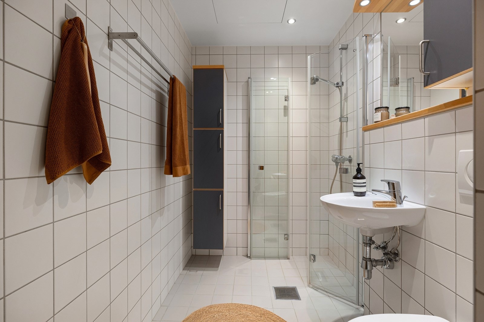 Rommet har servant, veggmontert toalett, veggmontert høyskap, speil med lys og skap, dusjvegger/hjørne og opplegg for vaskemaskin. Galleribilde