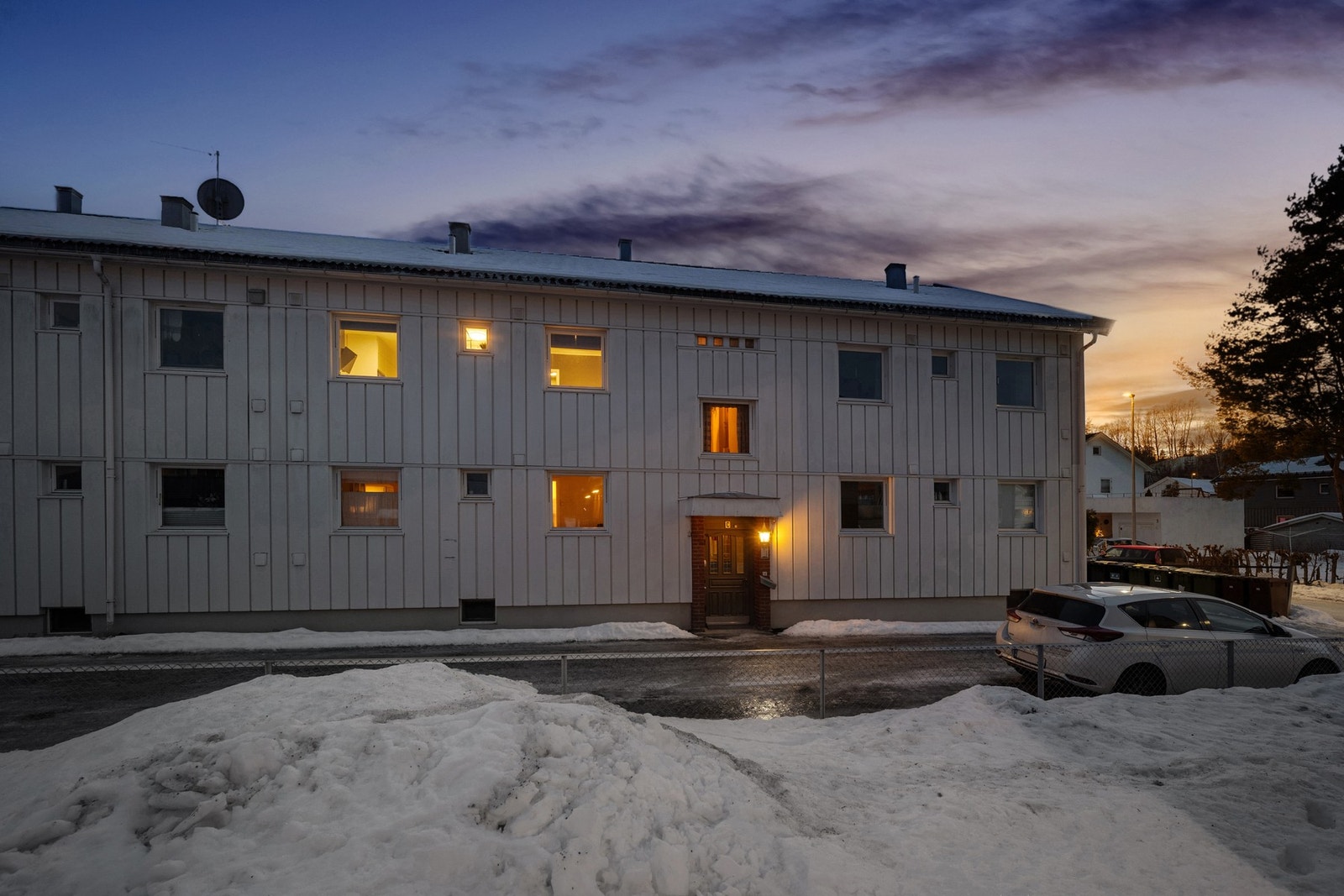 Forsiden av byggets inngang til leiligheten og parkeringsmulighet langs gjerdet ved inngangspartiet Galleribilde