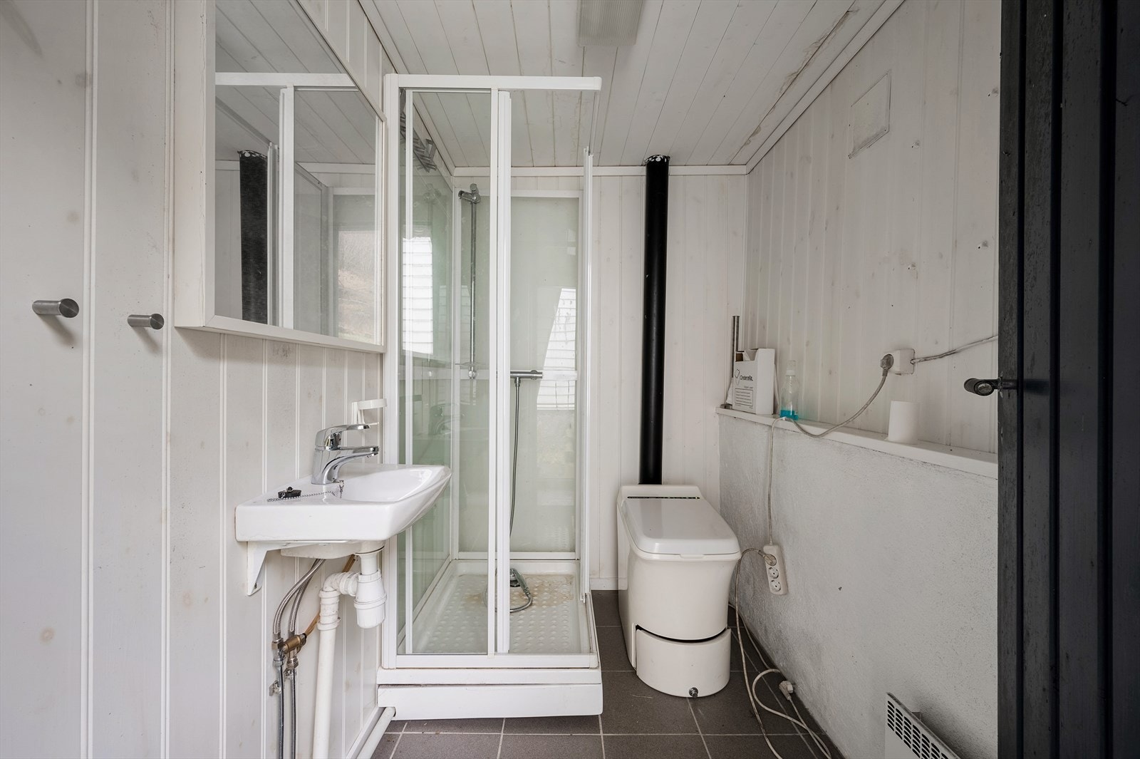 WC-rommet er innredet med vegghengt servant, speilskap, forbrenningstoalett og dusjkabinett. Galleribilde