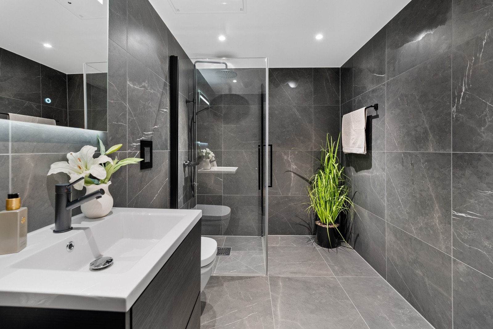 Bad to er i samme utførelse, med store, sorte vegg- og gulvfliser i marmormønster, vannbåren gulvvarme og downlights. Galleribilde