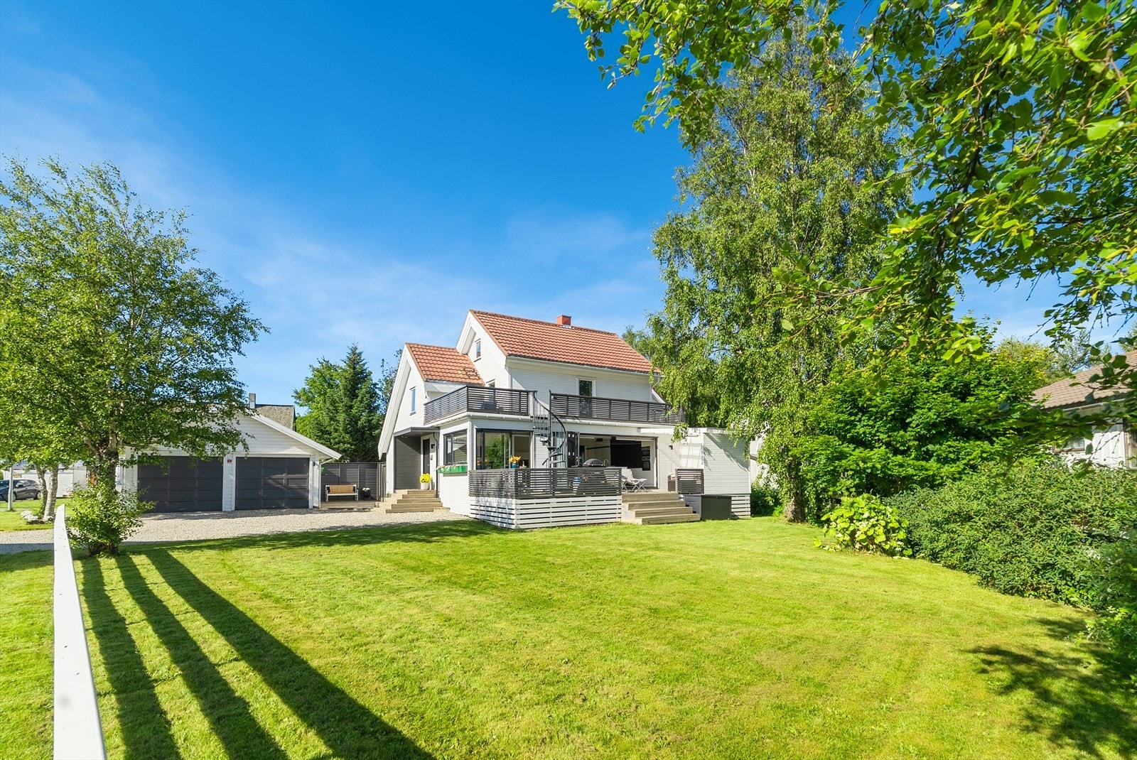 En stor og velstelt hage med vakre prydbusker og trær skaper en grønn og innbydende ramme. Galleribilde