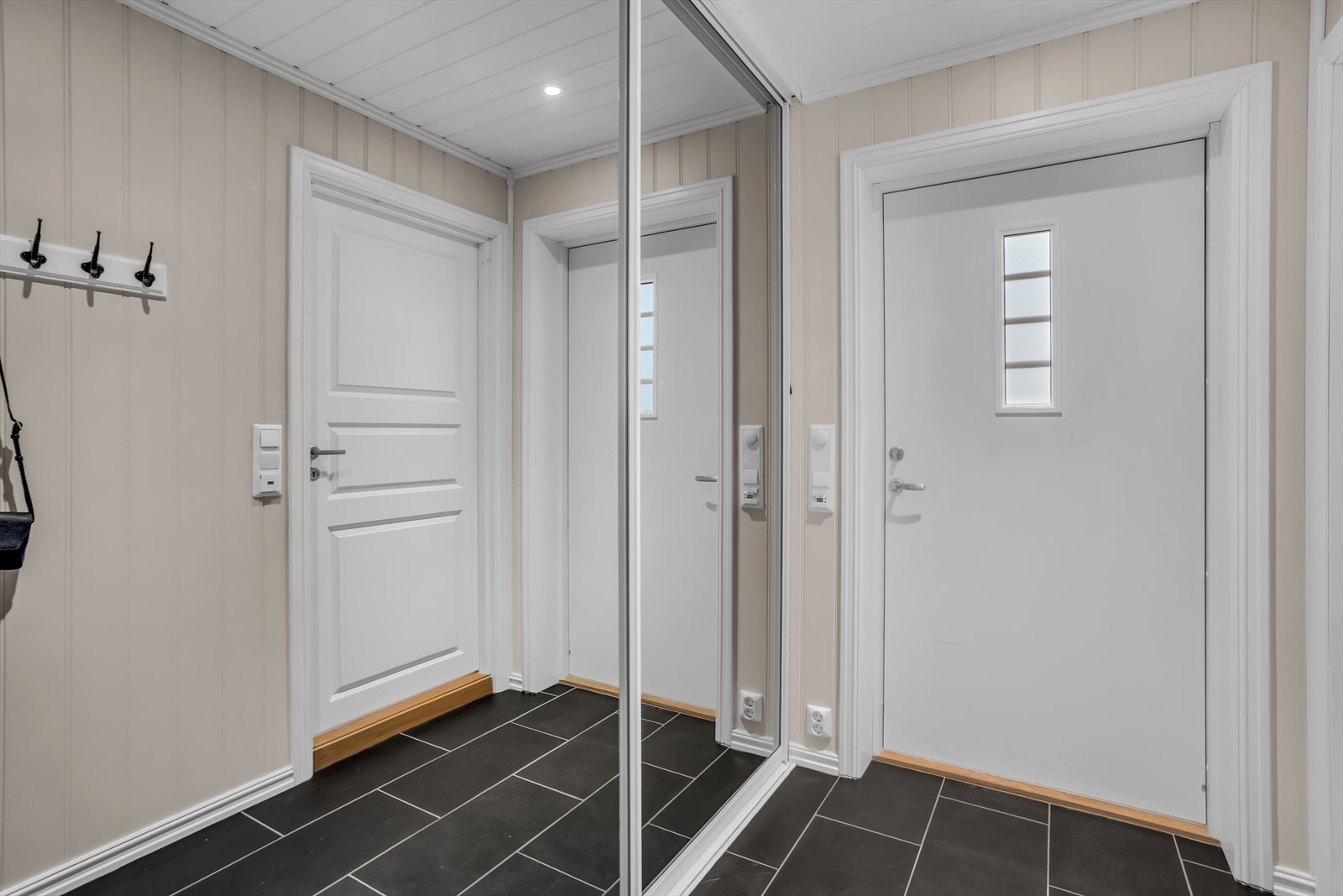 Velkommen inn i en lys entré med mørke gulvfliser og en stor skyvedørsgarderobe med speilfronter. Galleribilde