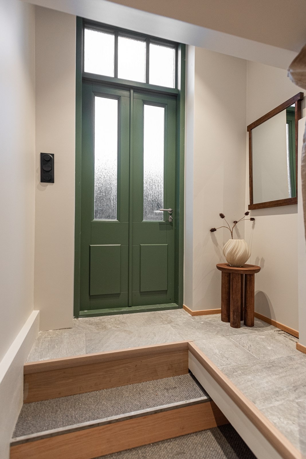 Entréen ligger adskilt fra resten av leiligheten, via noen trappetrinn, og har plass til oppheng av yttertøy og skostativ Galleribilde