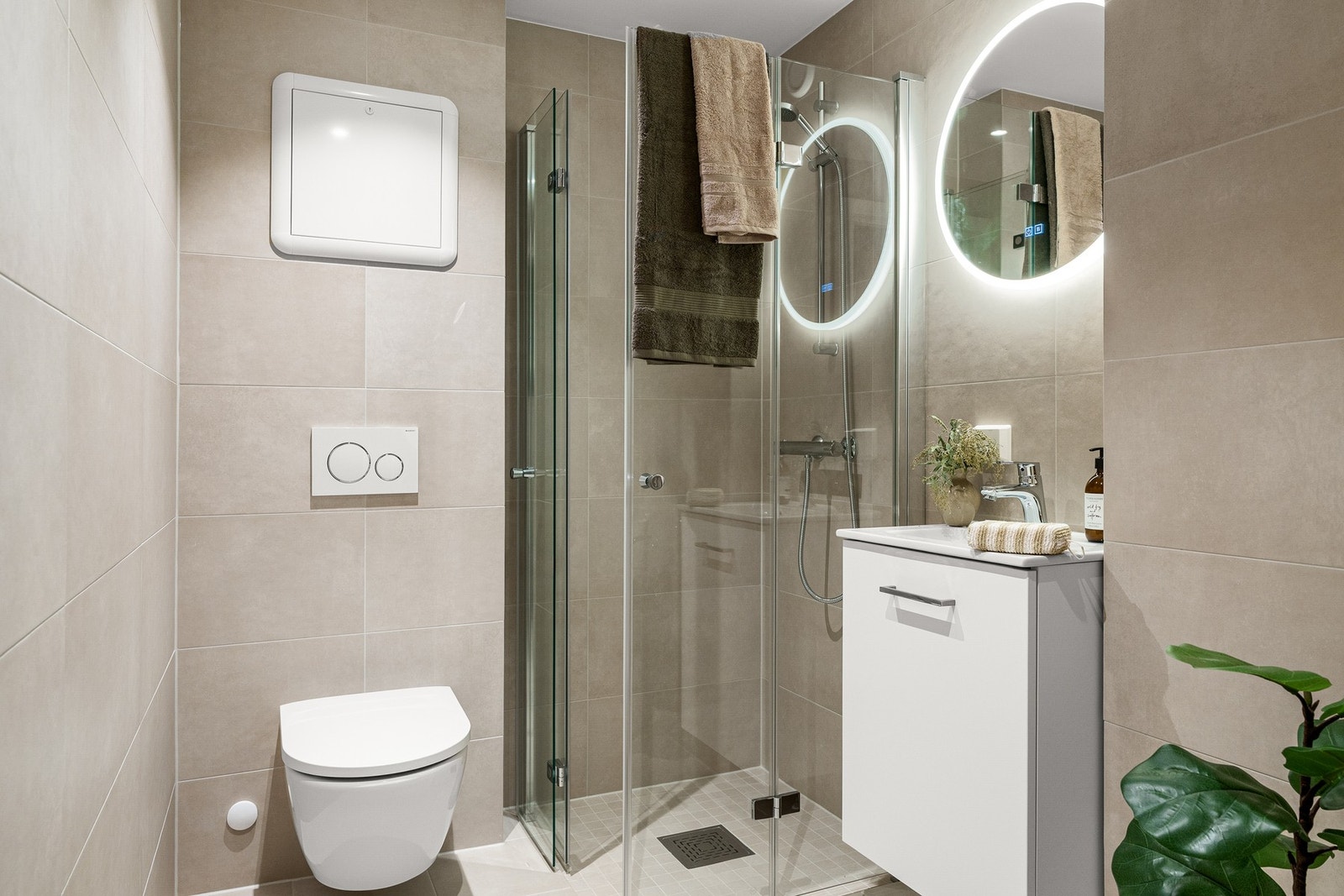 Lekkert flislagt bad fra 2025 med vegghengt toalett, dusj, baderomsinnredning og opplegg for vaskemaskin Galleribilde