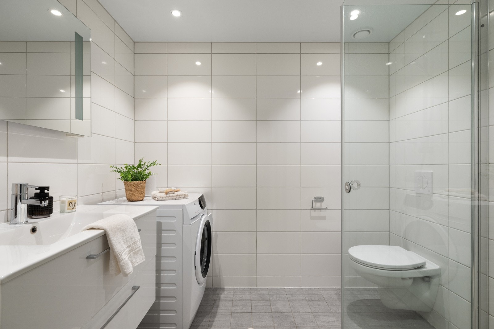 Badet i denne etasjen fremstår delikat og moderne, med lyse flislagte overflater på vegger og gulv, vegghengt toalett og dusjløsning med glassvegger. Galleribilde