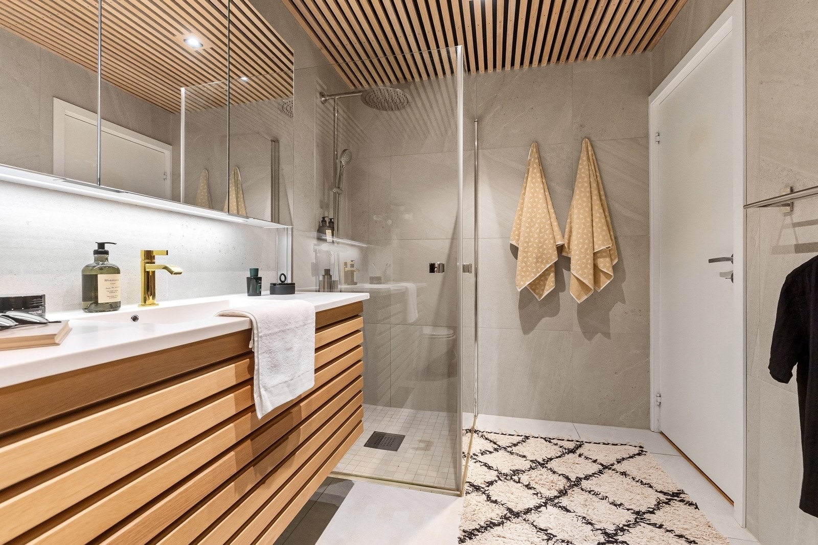 Badet er innredet med stor servant med underskuffer, speilskap, toalett, dusjhjørne med innfellbare glassvegger, samt opplegg for vaskemaskin. Galleribilde