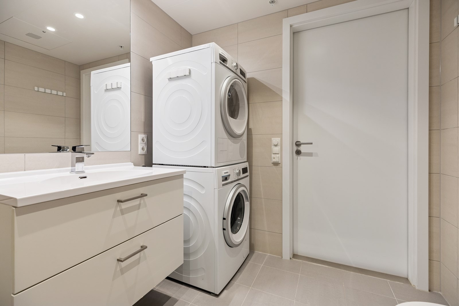 Badet har baderomsinnredning med benkeskap og veggskap med glatte fronter, speil over servant, vegghengt toalett, dusj med innfellbare vegger i herdet glass og opplegg for vaskemaskin. Galleribilde