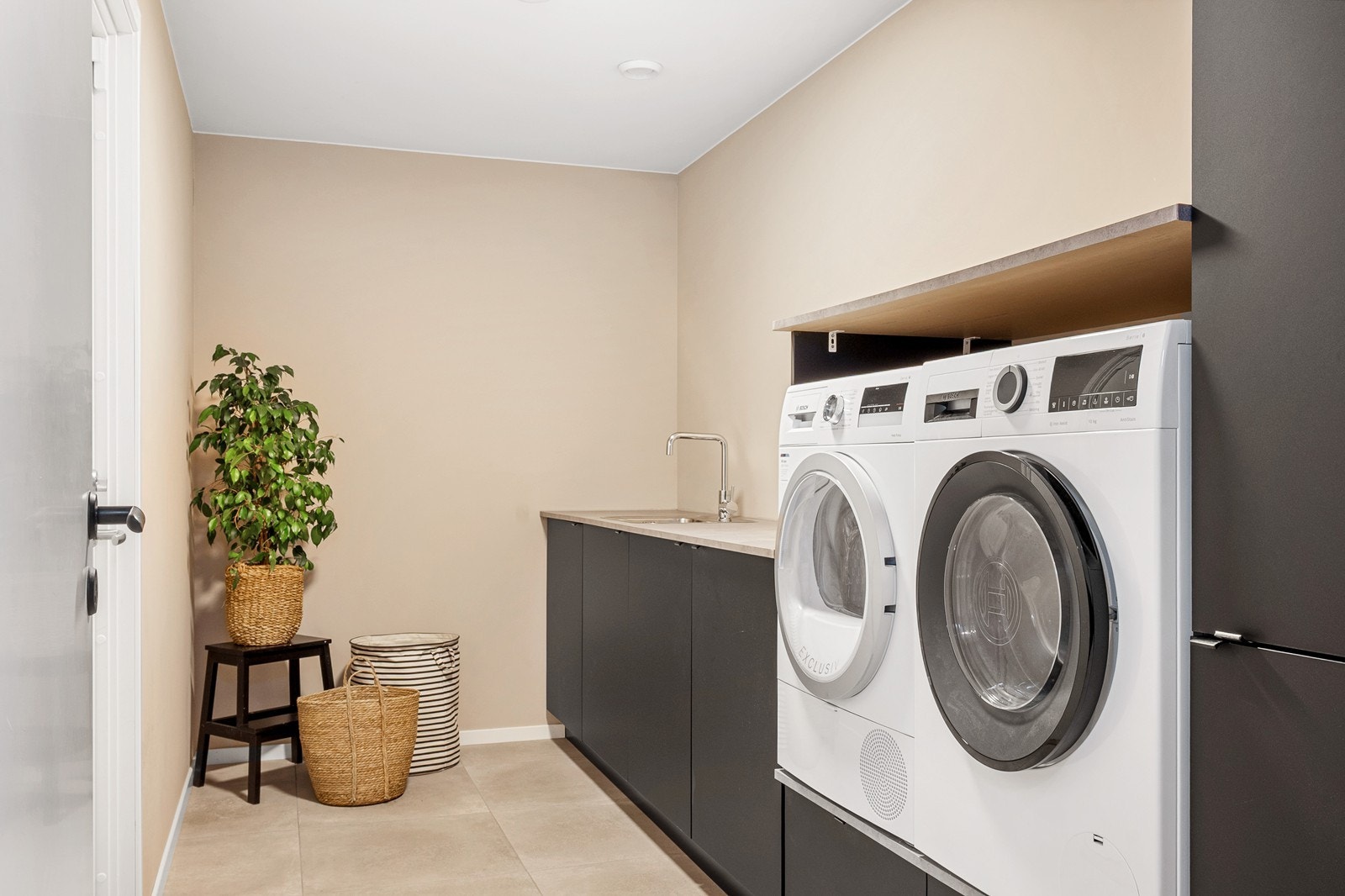 Vaskerommet har flislagt gulv, lyse overflater og praktisk innredning. Her finnes utslagsvask, røropplegg for vaskemaskin og tørketrommel, samt rikelig med skap- og benkeplass. Galleribilde