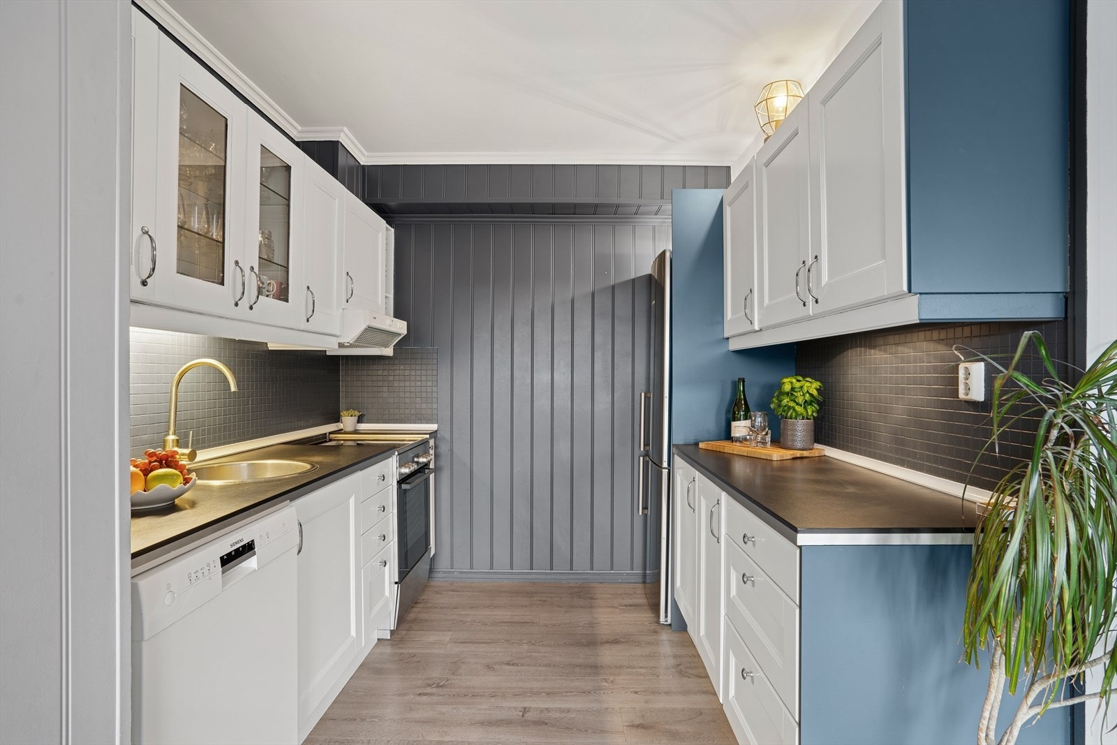 Kjøkkenet har innredning med hvite profilerte fronter, blå dekksider, sorte fliser over kjøkkenbenken. Benkeplaten er av laminat. Galleribilde