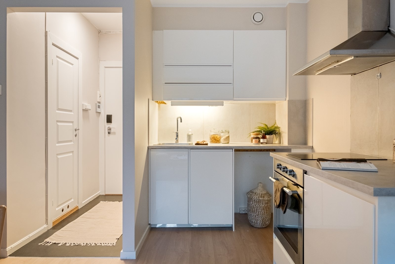 Tidsriktig glatt innredning fra IKEA, fliser over benk, armatur, laminat benkeplate med nedfelt stålkum og keramisk topp, integrert komfyr, oppvaskmaskin (smal type), kjøleskap. Det er kjøkkenventilator med kullfilter. Galleribilde