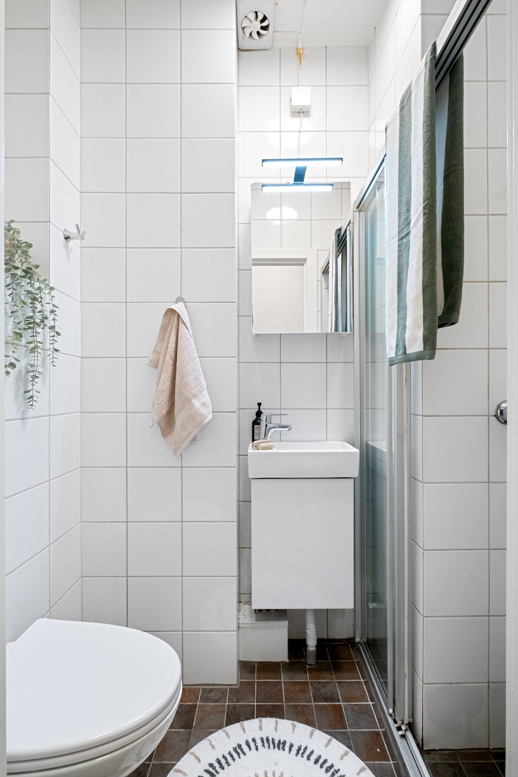 Flislagt baderom med varmekabler, avtrekk, speilskap med belysning, servant med innredning, dusj hjørne med skyvedør i glass, vegghengt toalet Galleribilde