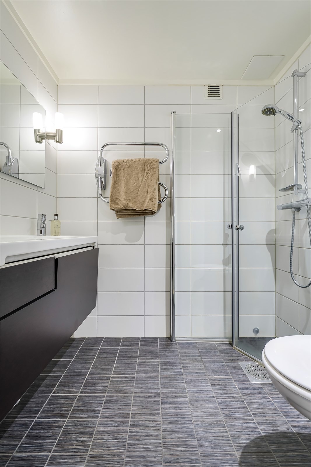 Pent, flislagt bad i moderne stil med moderne innredning, innfellbare dusjdører og varme i gulv. Galleribilde