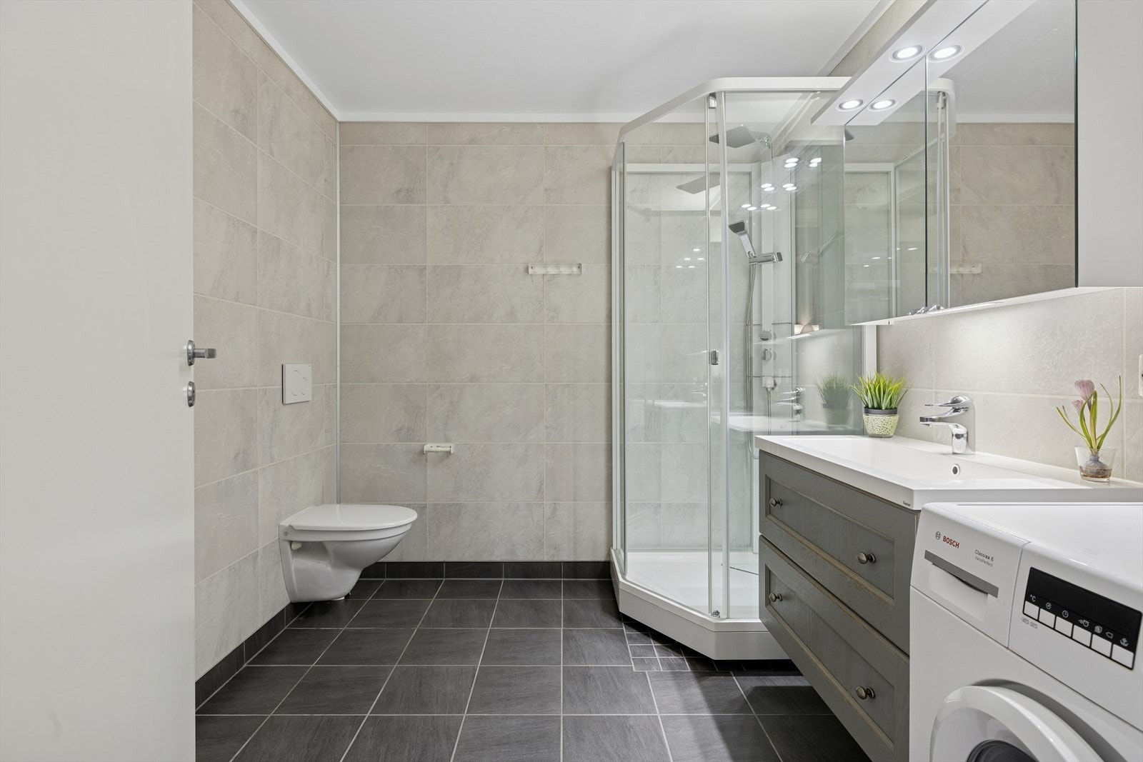 Badet er utstyrt med vegg hengt toalett, servant, opplegg til vaskemaskin og dusjkabinett. Galleribilde