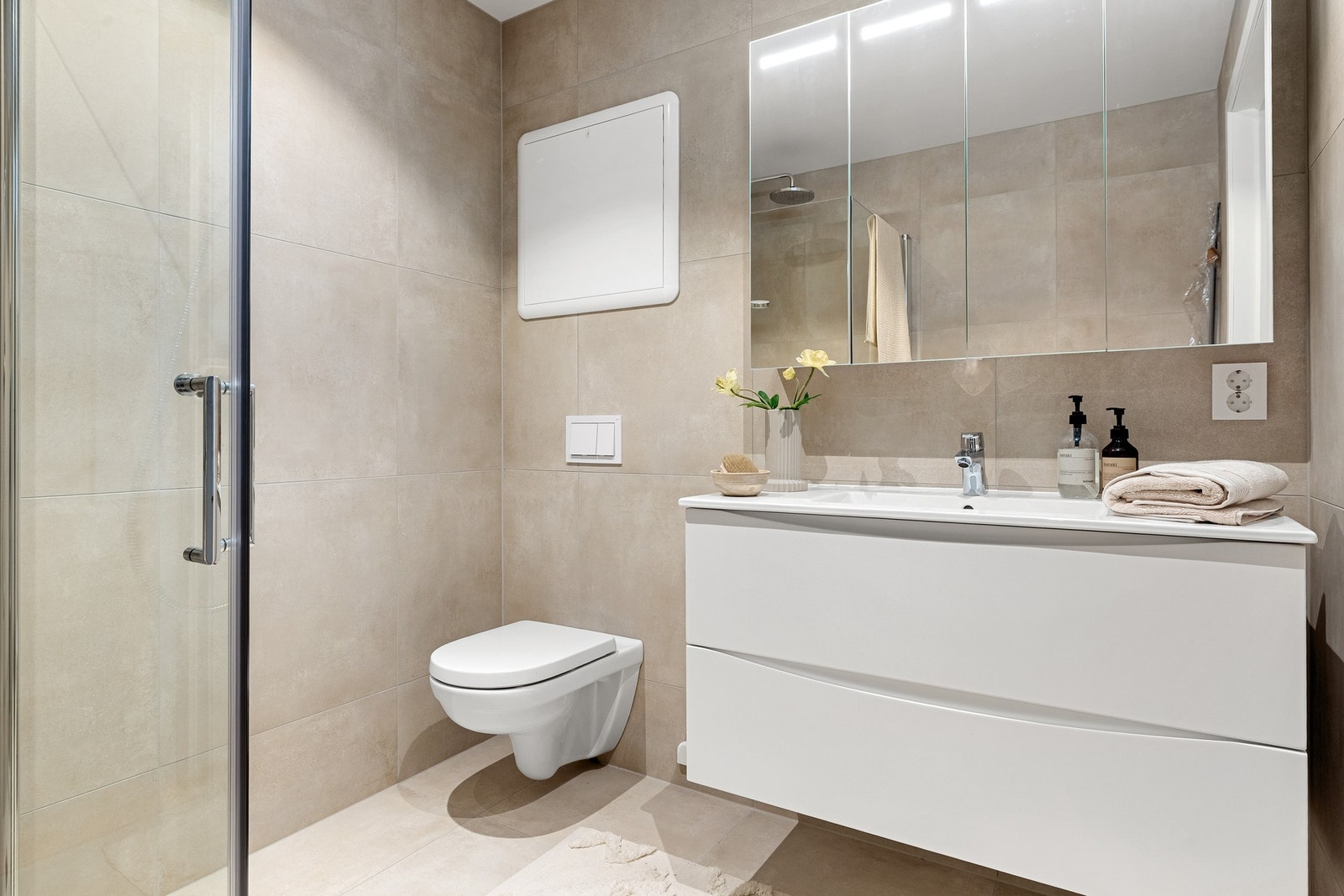 Det er innredet med vegghengt toalett, dusj med glassvegger, og baderomsmøblement med speil og belysning. Galleribilde