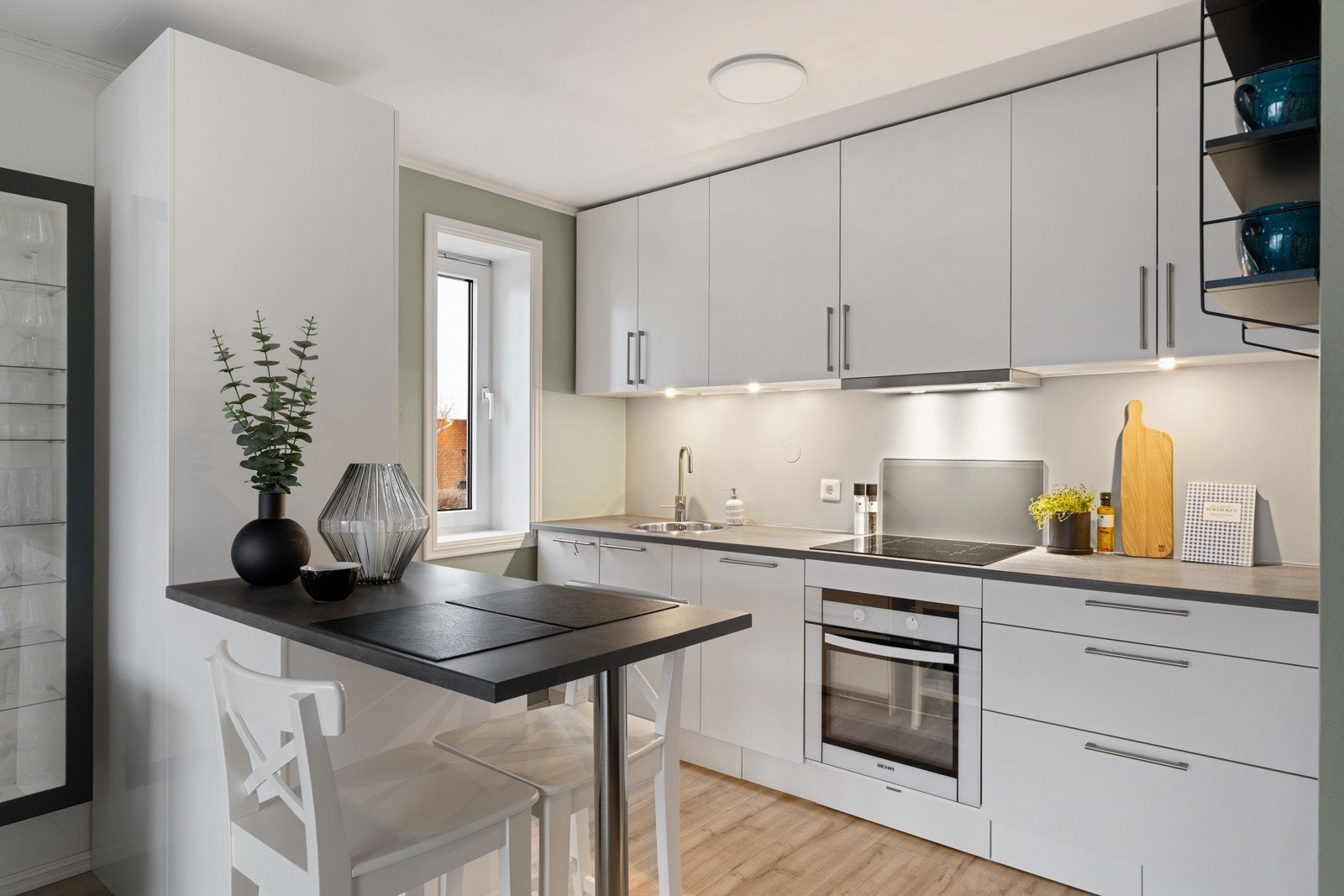 Lyst og moderne kjøkken med HTH-innredning på hoveddelen og en praktisk barløsning, samt integrert kjøl- og fryseskap fra IKEA på motsatt side. Galleribilde