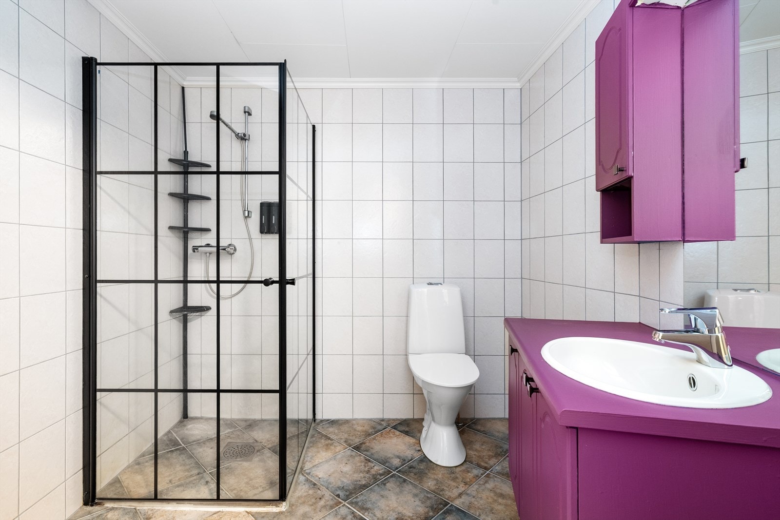 Leiligheten har et romslig, helfliset bad med varmekabler i gulvet. Her er det innredning med skap og nedfelt servant, samt dusjhjørne med dusjvegger og sorte profiler. Galleribilde