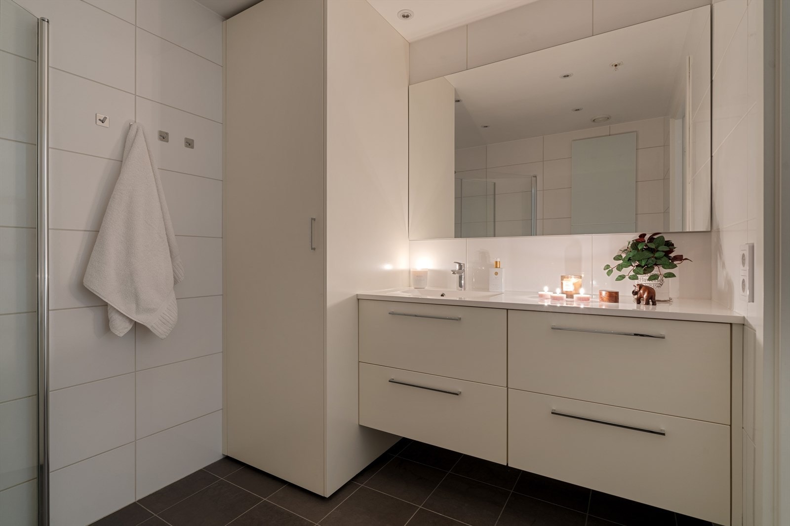 Badet er helfliset med varmekabler i gulvet. Det inneholder en smart nisje med opplegg for vaskemaskin/tørketrommel, samt dusj med innfellbare dusjdører, vegghengt toalett, samt baderomsinnredning med speil over. Galleribilde