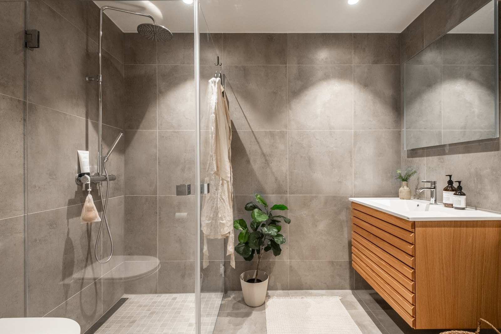 Badet fremstår moderne og stilrent, med store fliser, innfellende belysning og en romslig dusjsone med glassvegger og regndusj. Her finner du også veggmontert toalett, opplegg for vaskemaskin og plass til tørketrommel. Galleribilde