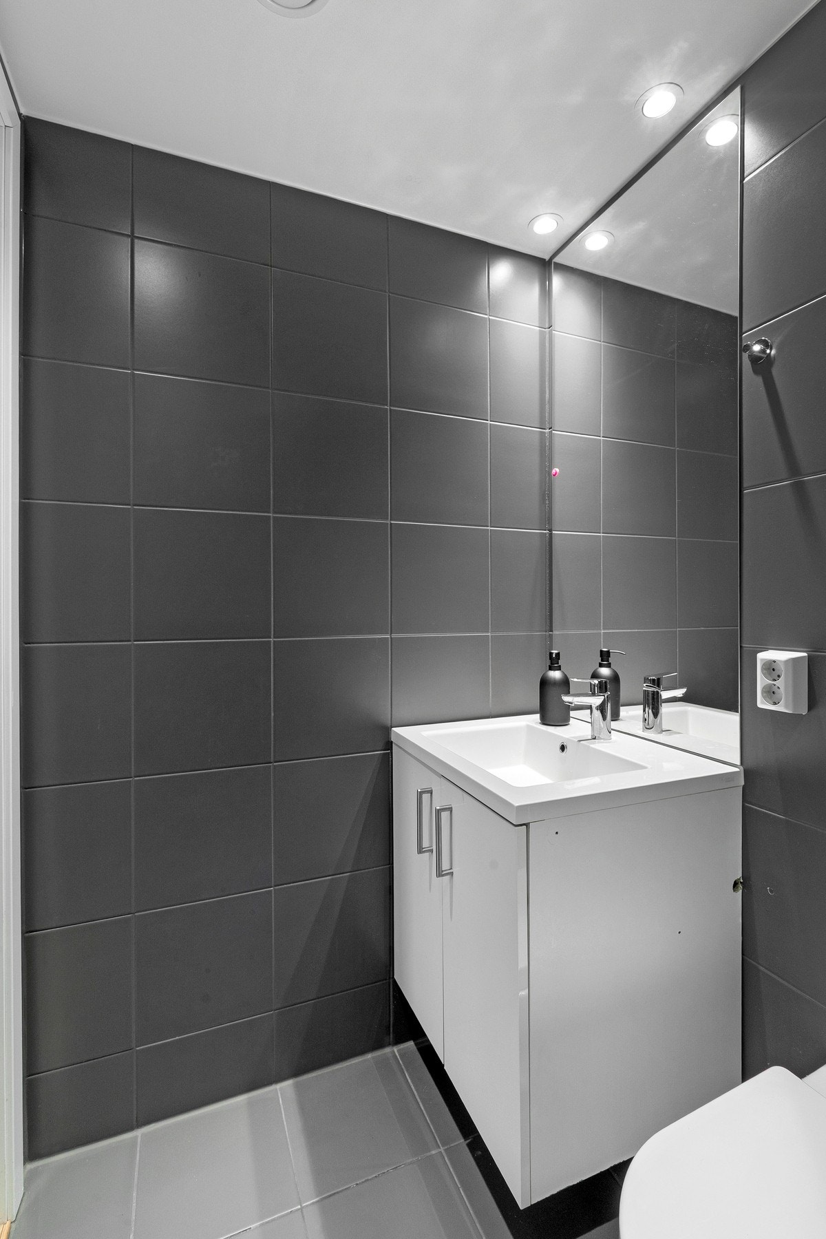 Innredet med veggmontert toalett, dusjdører i herdet glass, veggspeil med overliggende belysning, baderomsinnredning med høyglans fronter og heldekkende servant. Galleribilde