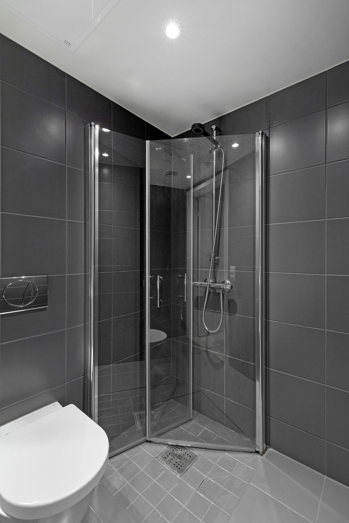 Innredet med veggmontert toalett, dusjdører i herdet glass, veggspeil med overliggende belysning, baderomsinnredning med høyglans fronter og heldekkende servant. Galleribilde