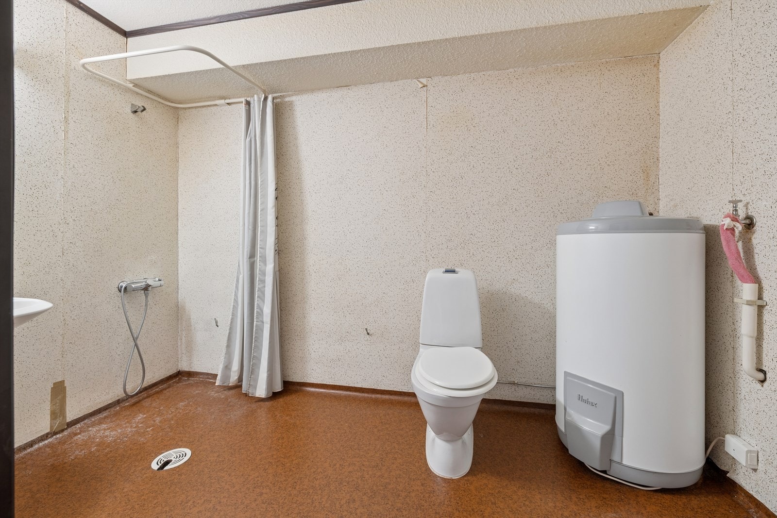 Baderommet har belegg på gulvet og tapet på veggene, med en dusjsone skjermet av forheng. Badet har behov for omfattende oppgraderinger for å oppfylle dagens krav. Galleribilde