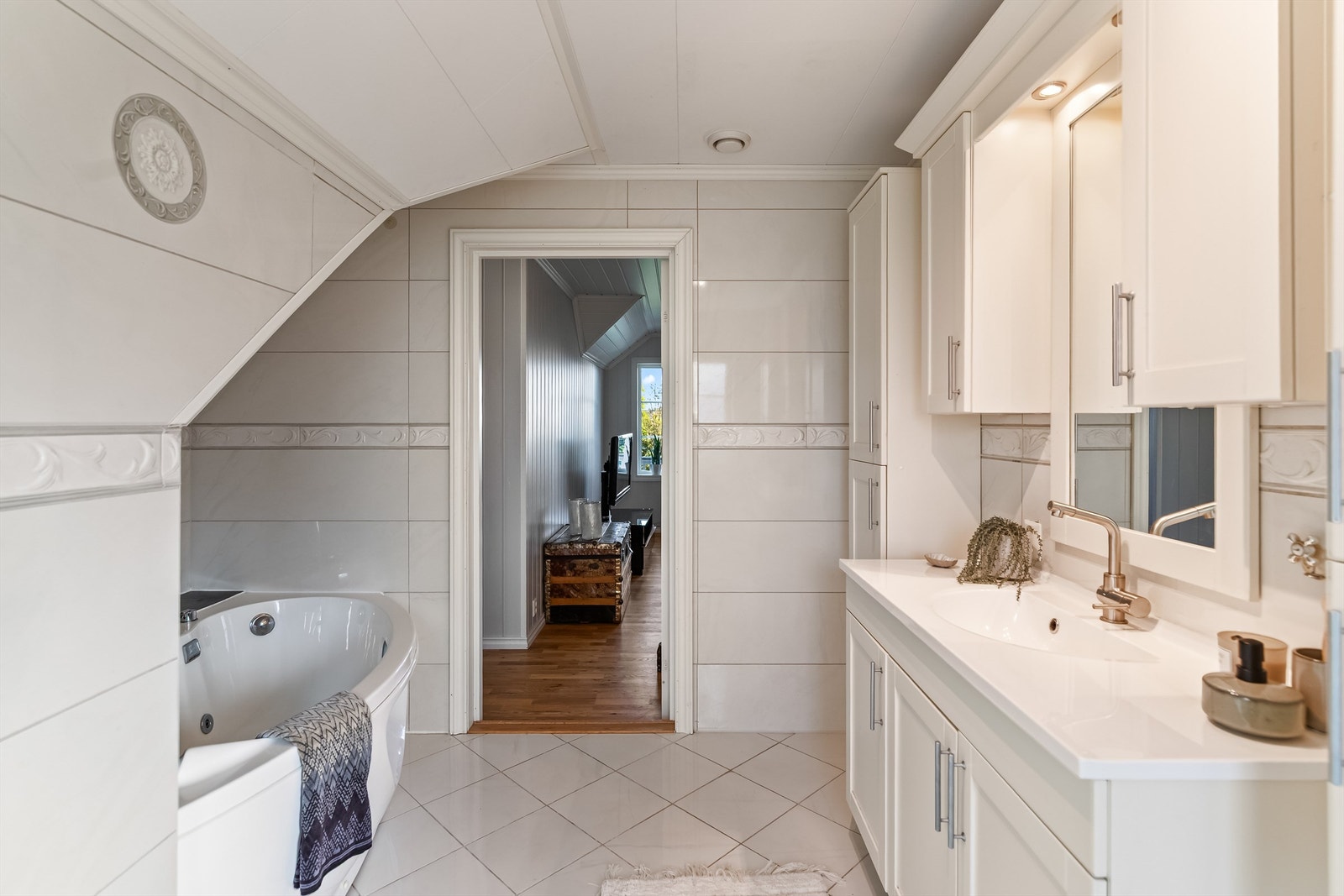 Det er montert vegghengte skap og baderomsinnredning med heldekkende servant. Speil, skap, overlys og stikkontakt er montert på vegg over servanten. Badekar og vegghengt toalett. Galleribilde