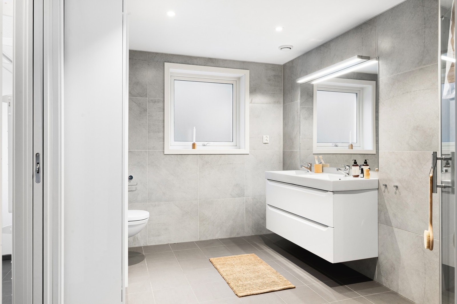 Det er innredet med et vegghengt toalett, dusj med glassvegger og baderomsinnredning med dobbel servant, speil og belysning. Galleribilde