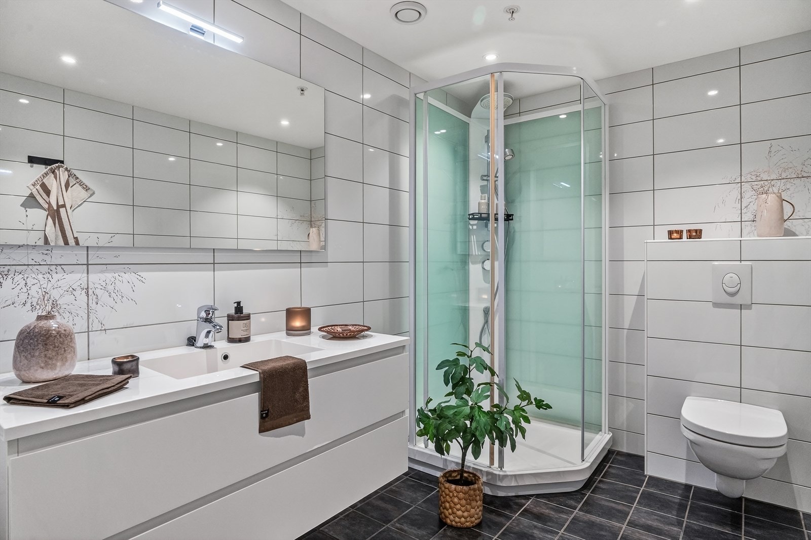 Pent helfliset bad som inneholder baderomsinnredning m/servant, dusjkabinett og vegghengt toalett. Galleribilde