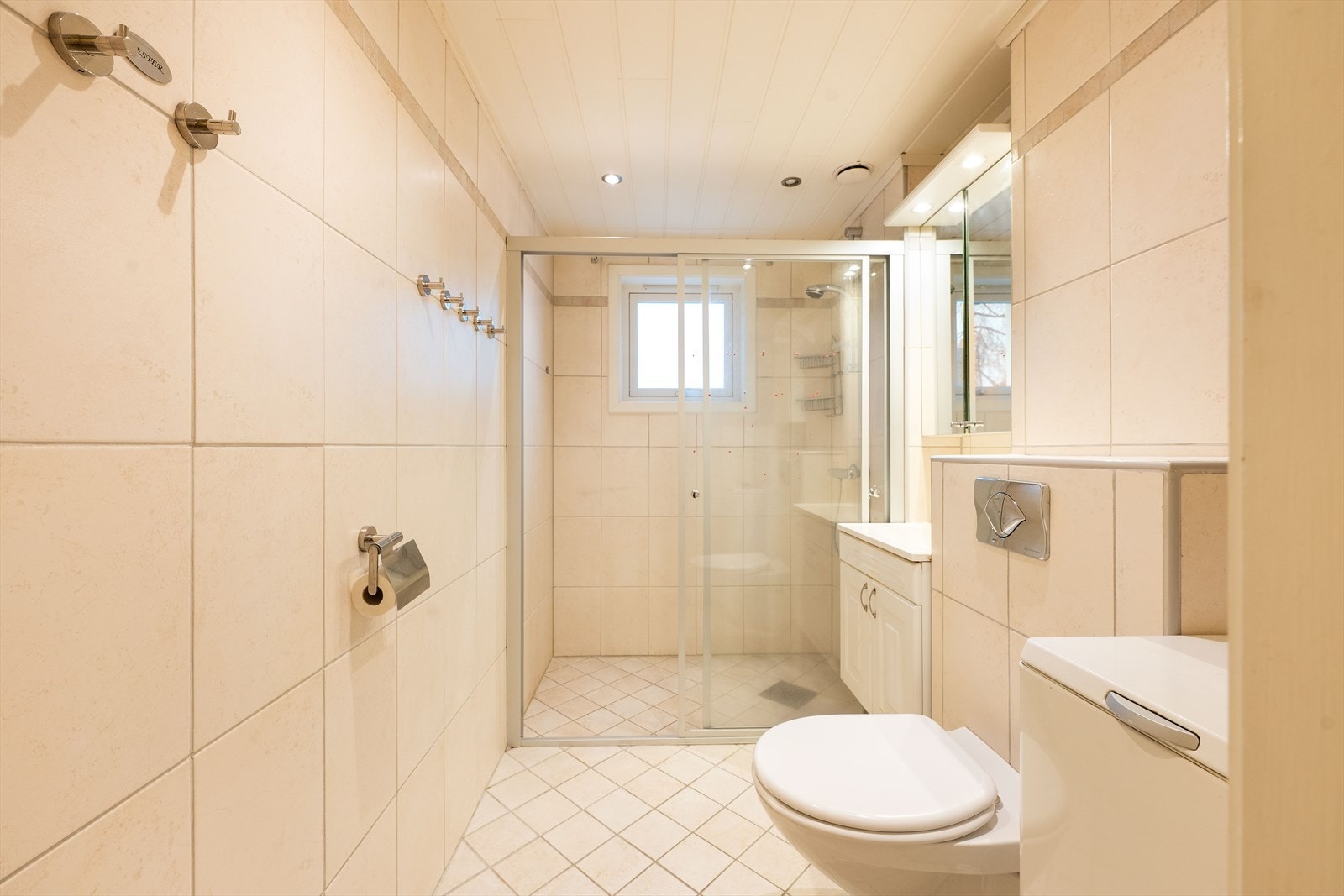 Rommet har servant med profilerte fronter, veggmontert toalett og en romslig dusj. Galleribilde